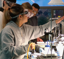 A female student wearing safety glasses works in a lab